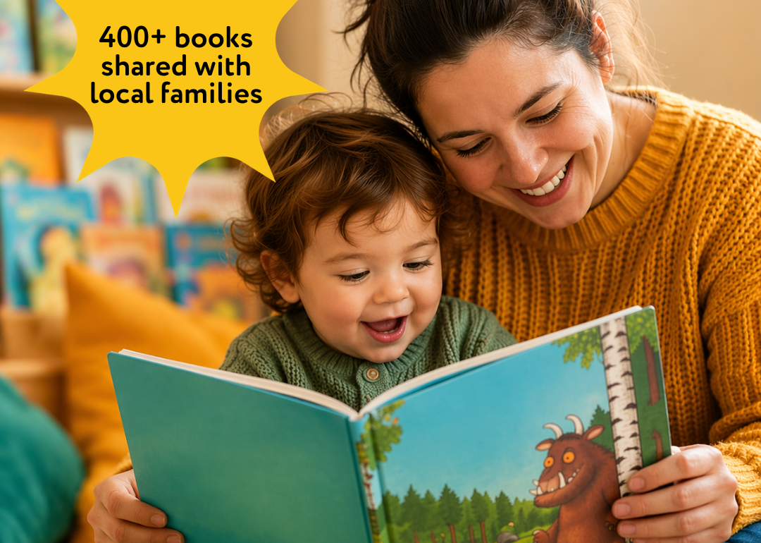 Warm, close-up image of a smiling mother sitting with her young child on the floor, reading a colourful picture book together in a cosy, softly lit room, with bookshelves blurred in the background. Overlayed text stating over 400 books have been shared with local families