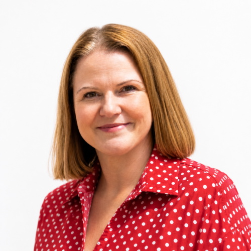 Smiling woman with shoulder-length light brown hair, wearing a red polka dot blouse, in a clean, well-lit headshot against a plain white background.